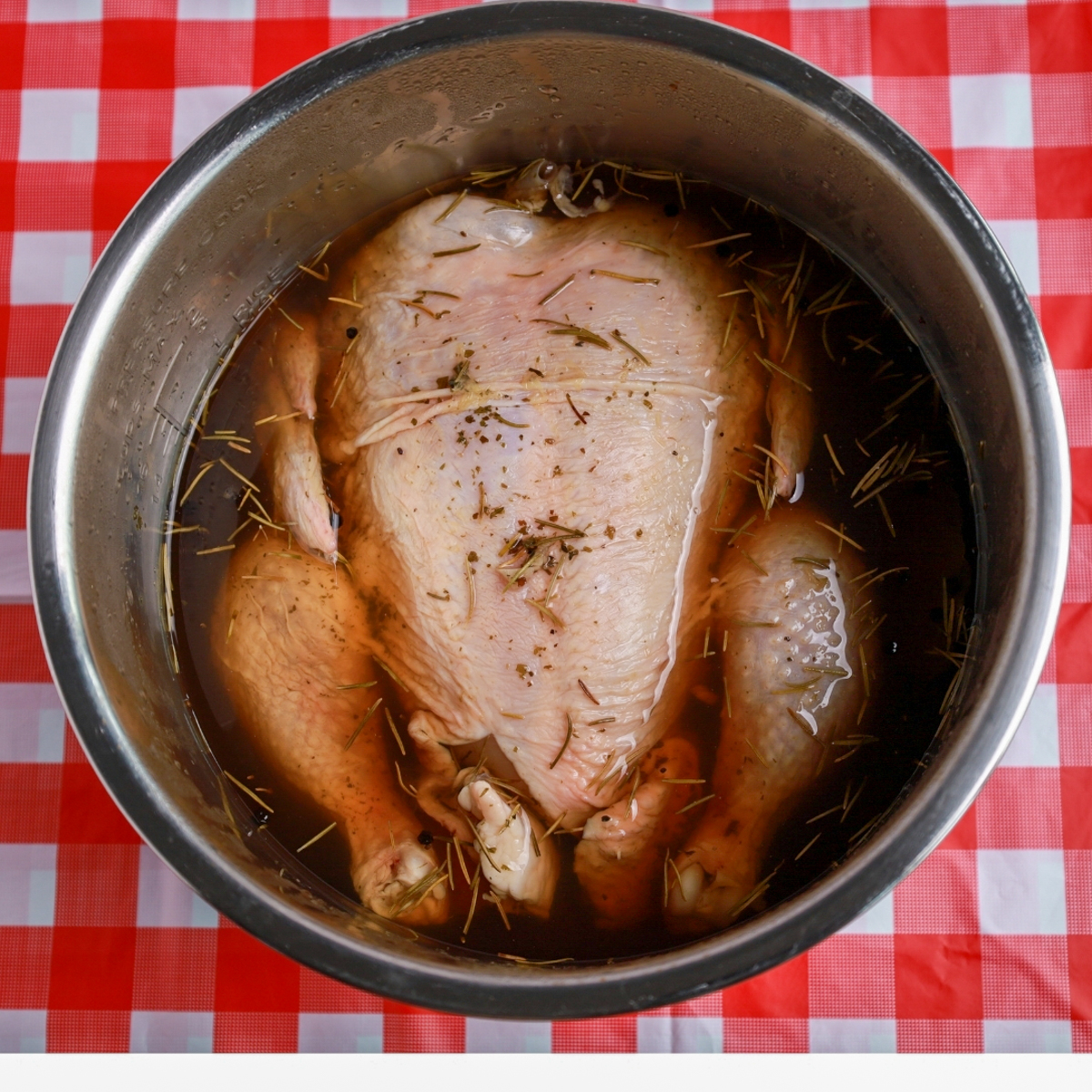 Whole chicken soaking in a savory brine with herbs and spices.