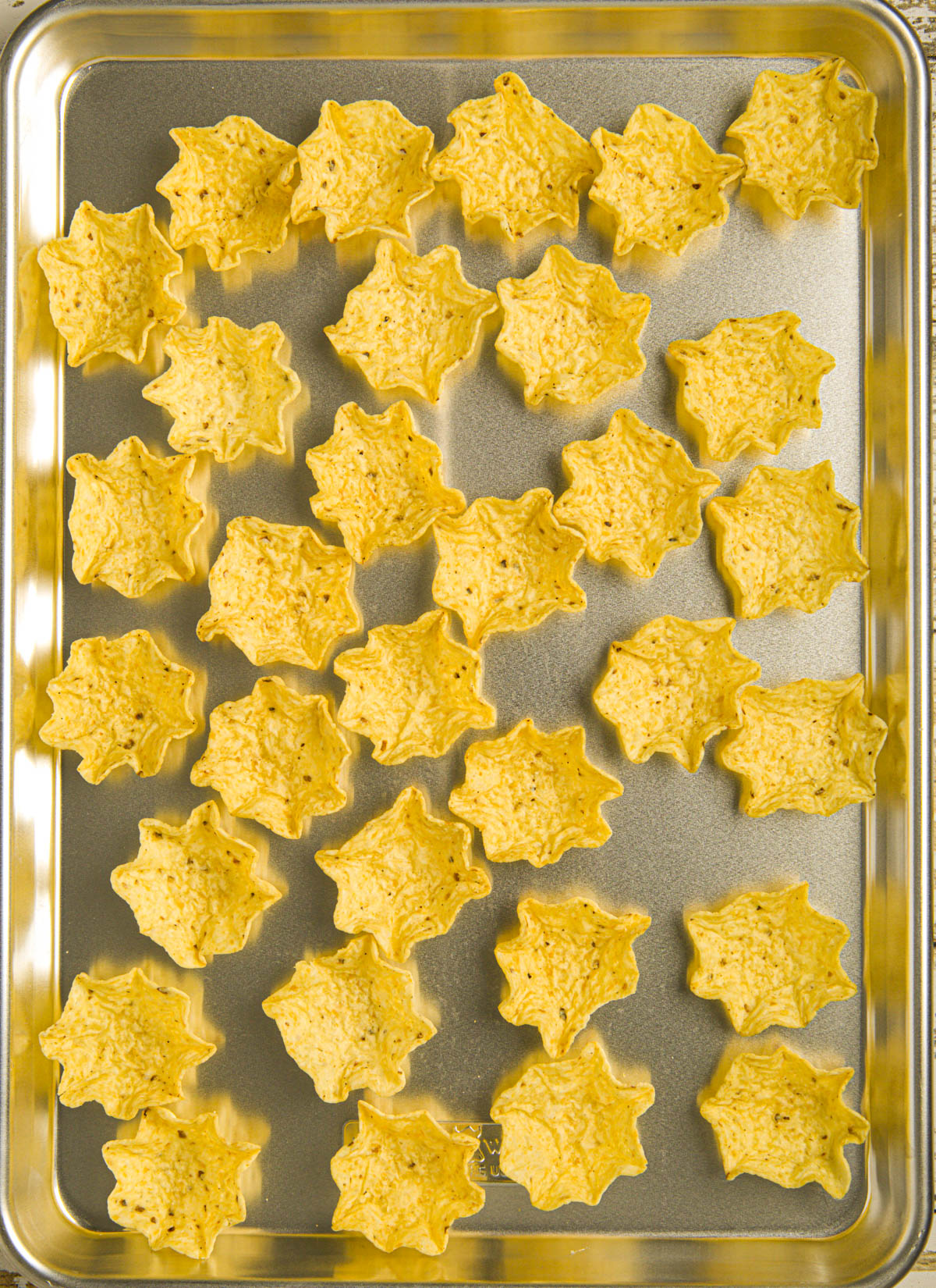A close-up of crispy tortilla scoops chips piled on a baking sheet, ready to be assembled with flavorful toppings.