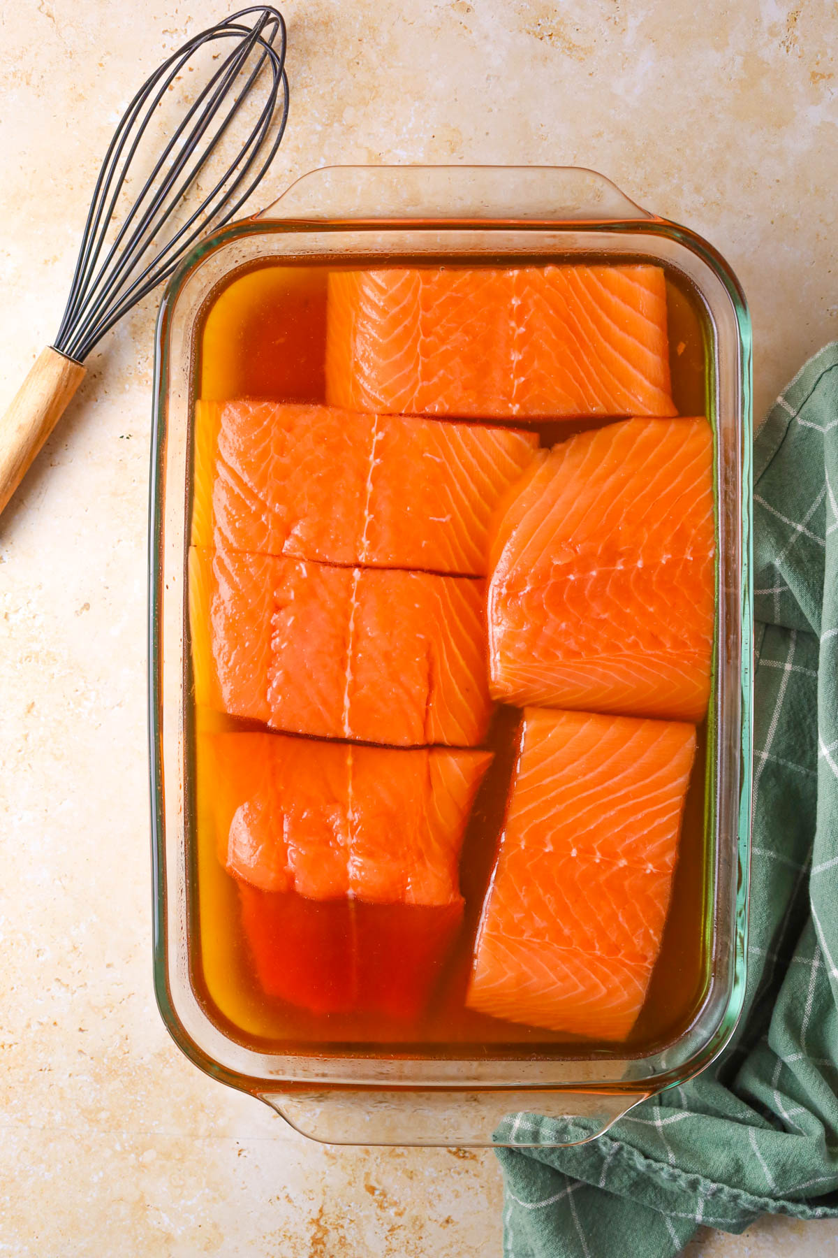 A raw salmon fillet soaking in a brine mixture with herbs and spices.