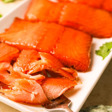 A flaky, perfectly smoked salmon fillet being lifted with a fork, surrounded by other salmon fillets on the plate.