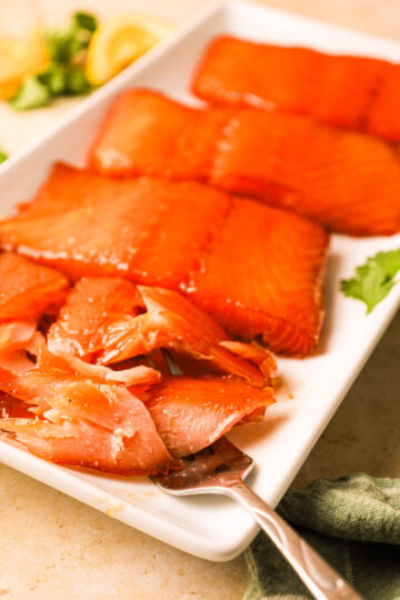 A flaky, perfectly smoked salmon fillet being lifted with a fork, surrounded by other salmon fillets on the plate.
