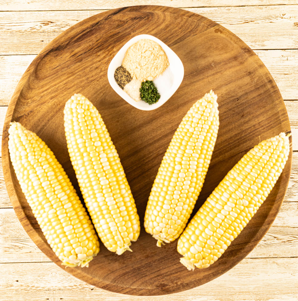 Raw corn on the cob with a selection of spices arranged beside it, ready to be seasoned and grilled.