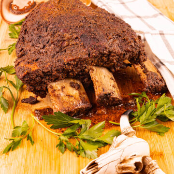 Smoked dino beef ribs, glistening with rich seasonings, with the bones starting to fall away, resting on a cutting board.