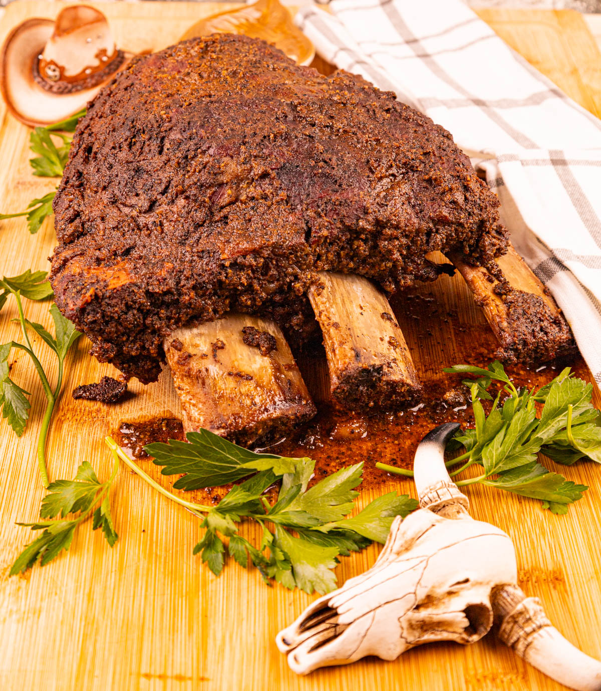 Smoked dino beef ribs, glistening with rich seasonings, with the bones starting to fall away, resting on a cutting board.