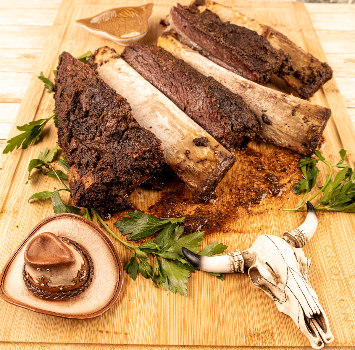 Beef dino ribs on a cutting board, with the bones starting to fall out, tender and ready to be served.
